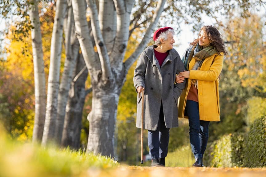Granddaughter walking with senior woman in park wearing winter c